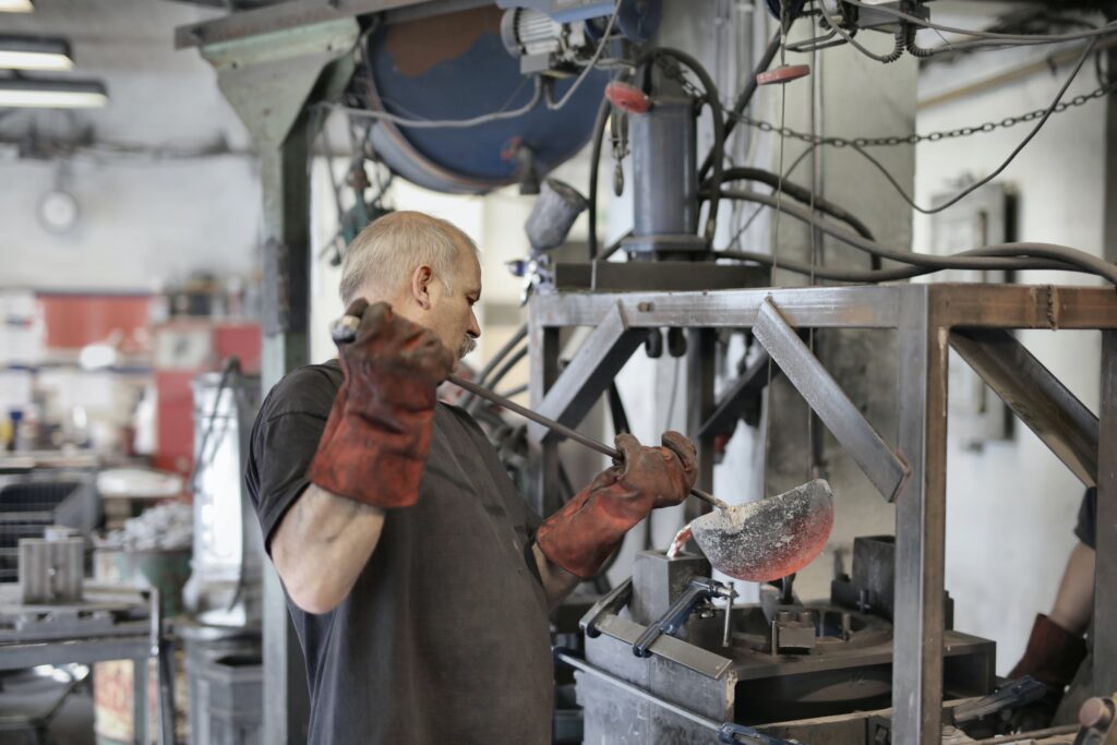 Side view of senior white hair worker in apron and heavy duty gloves melting detail from iron